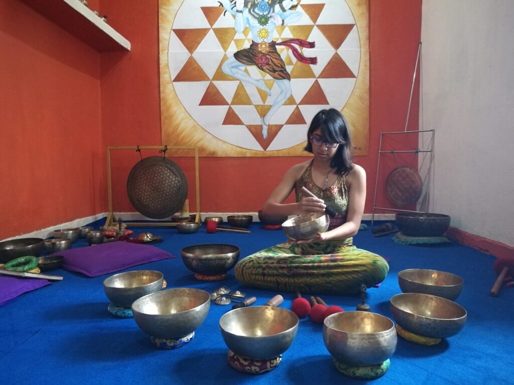 child of the earth playing singing bowls in front of a shiva poster